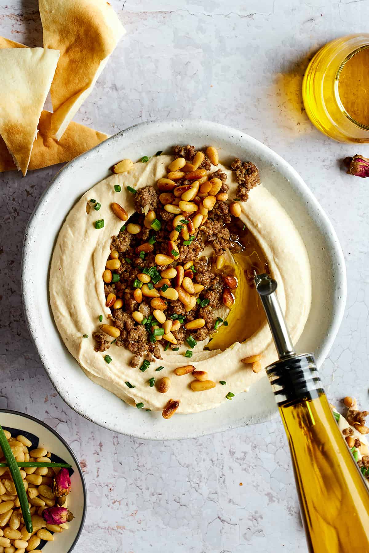 Olive oil being drizzled over a bowl of hummus with ground beef. 