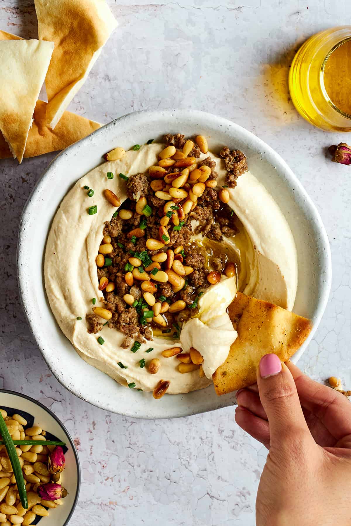 A bowl of hummus with ground beef with a pita chip being dipped in. 