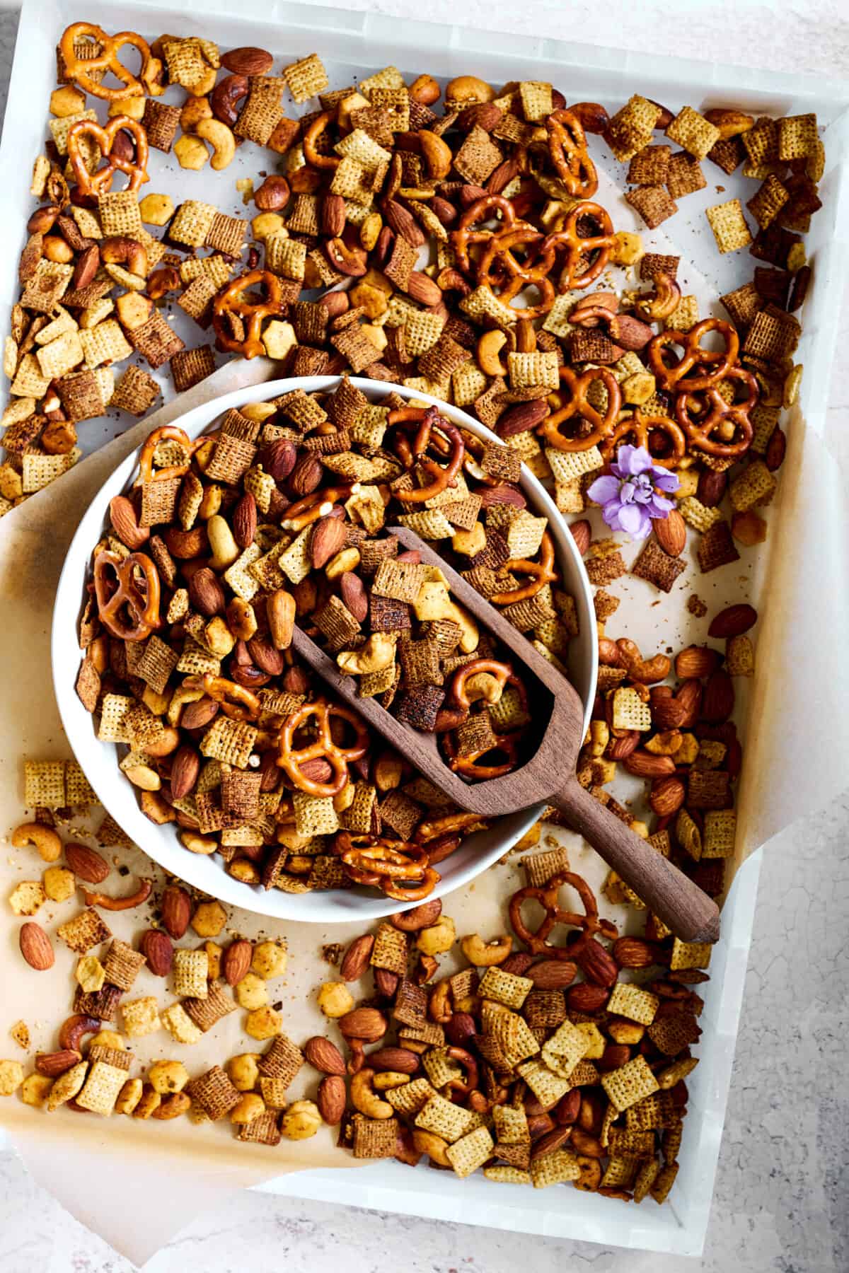 A bowl of spicy Chex mix on a baking sheet of the mix. 