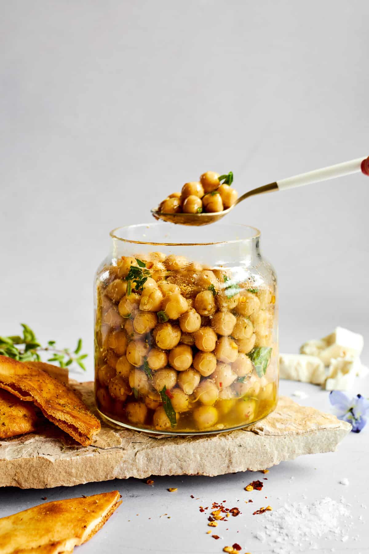 A spoonful of marinated chickpeas being lifted from a jar. 