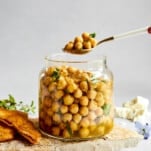 A spoon lifting a scoop of marinated chickpeas from a jar.