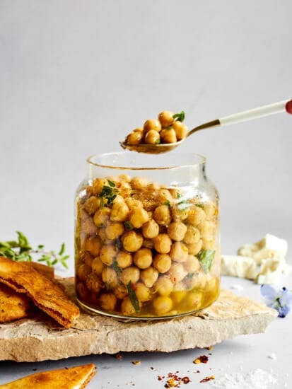 A spoon lifting a scoop of marinated chickpeas from a jar.