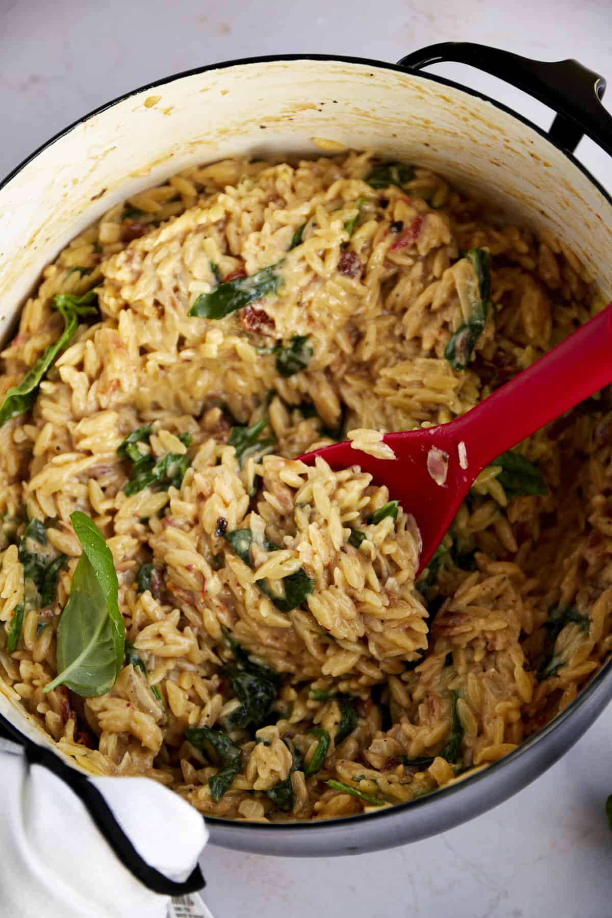 A pot of creamy tuscan orzo pasta being stirred with a spatula. 