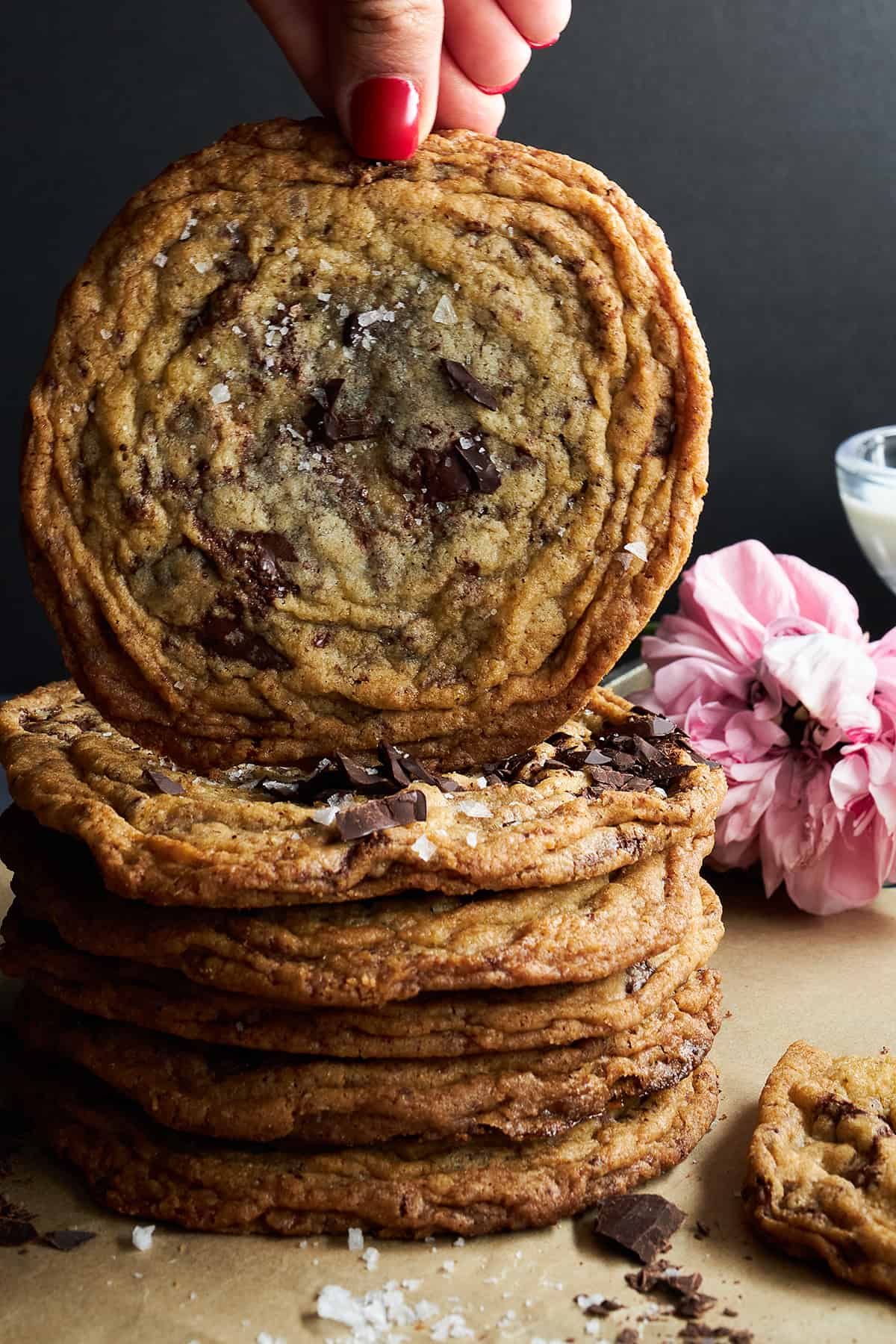 A hand lifting a banging chocolate chip cookie off a stack of cookies. 
