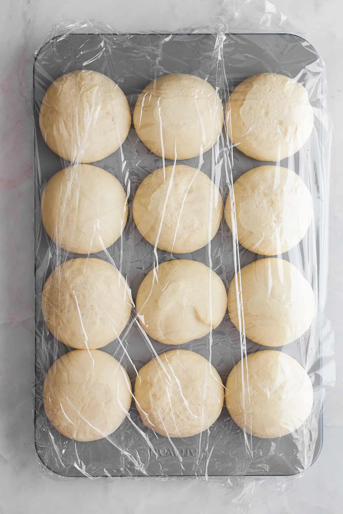 Risen bread rolls in a muffin tin.