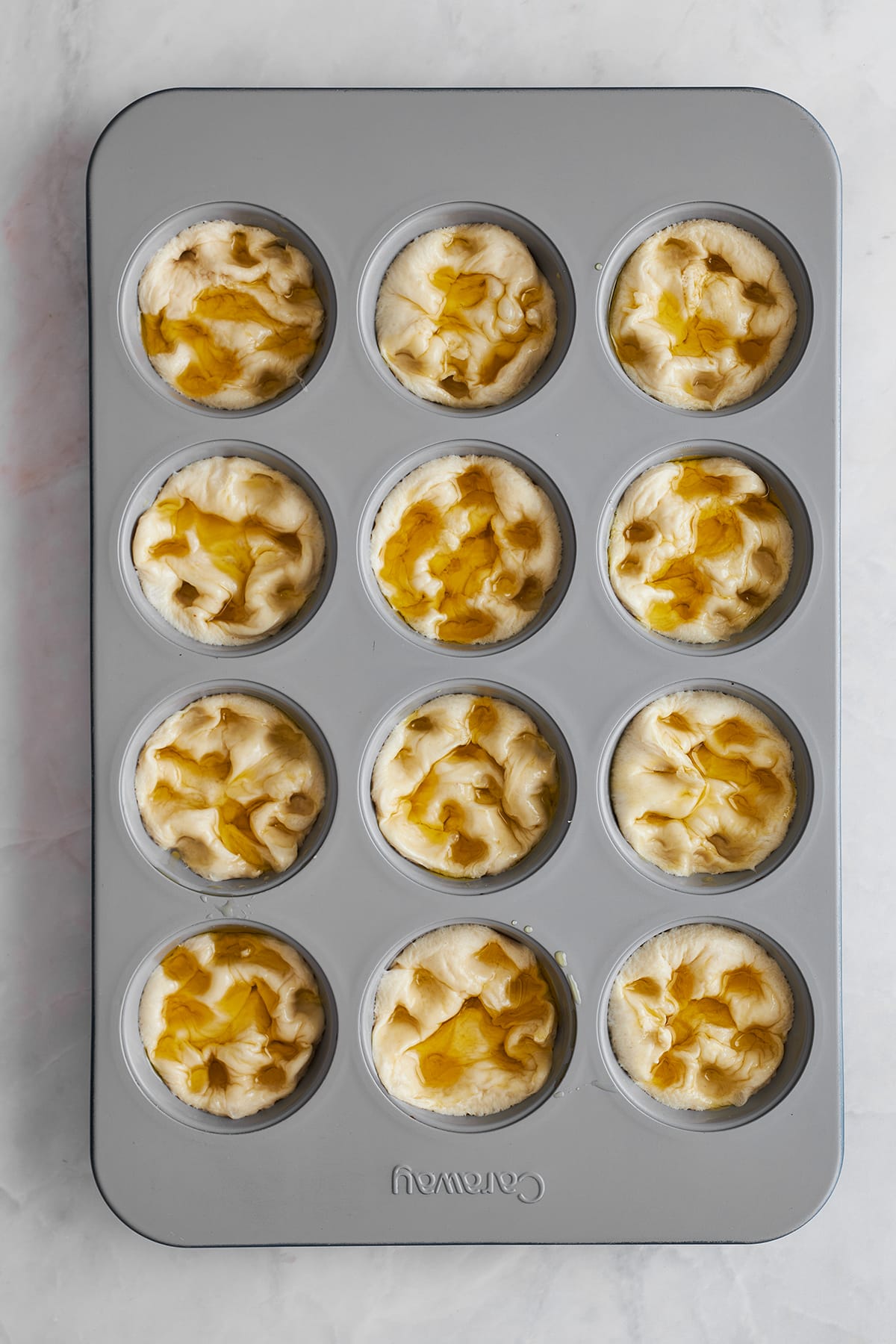 Indented bread rolls in a muffin tin topped with olive oil. 