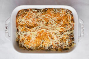 Cheese and beef being layered on slider buns in a baking dish.