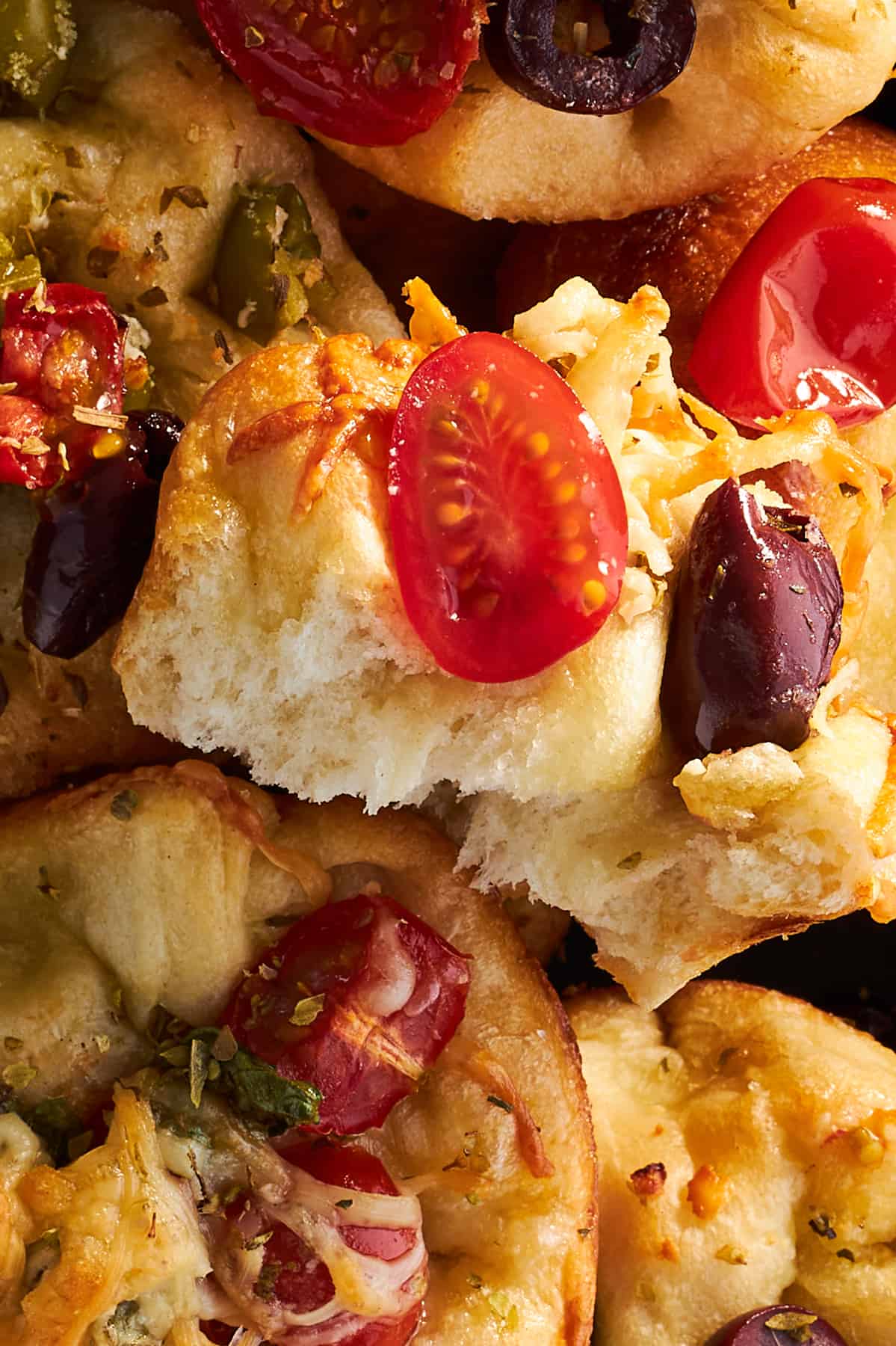 Close up image of focaccia muffins topped with tomatoes, olives, and cheese. 