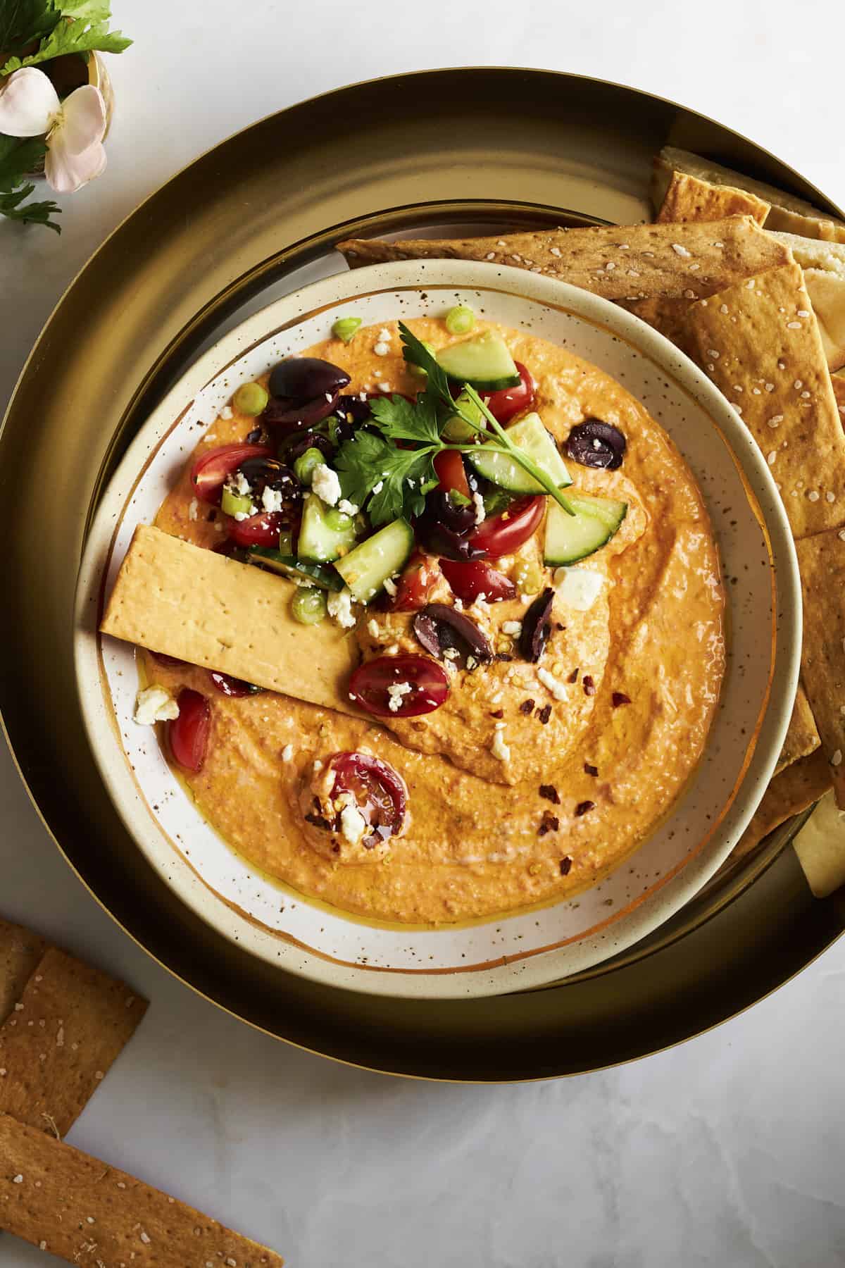 A bowl of spicy feta dip with veggies on top and crackers for dipping. 