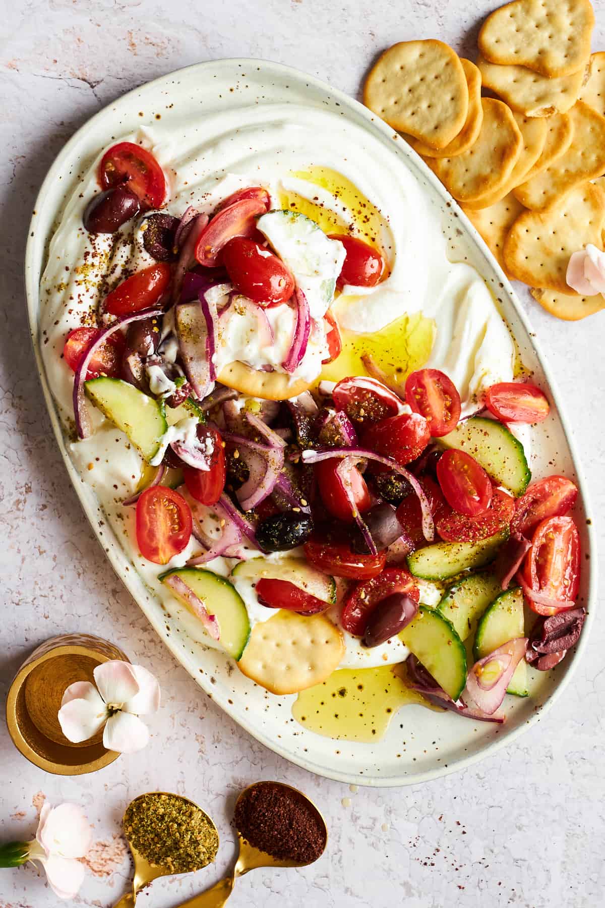 A platter of Greek salad dip with crackers on the side.