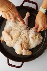 Cuts being made in the sides of a spatchcock chicken.