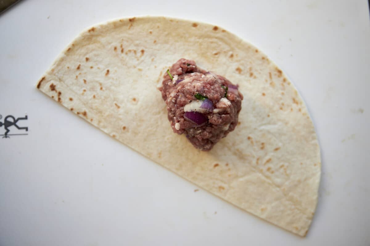 Raw ground beef in the center of a tortilla half. 