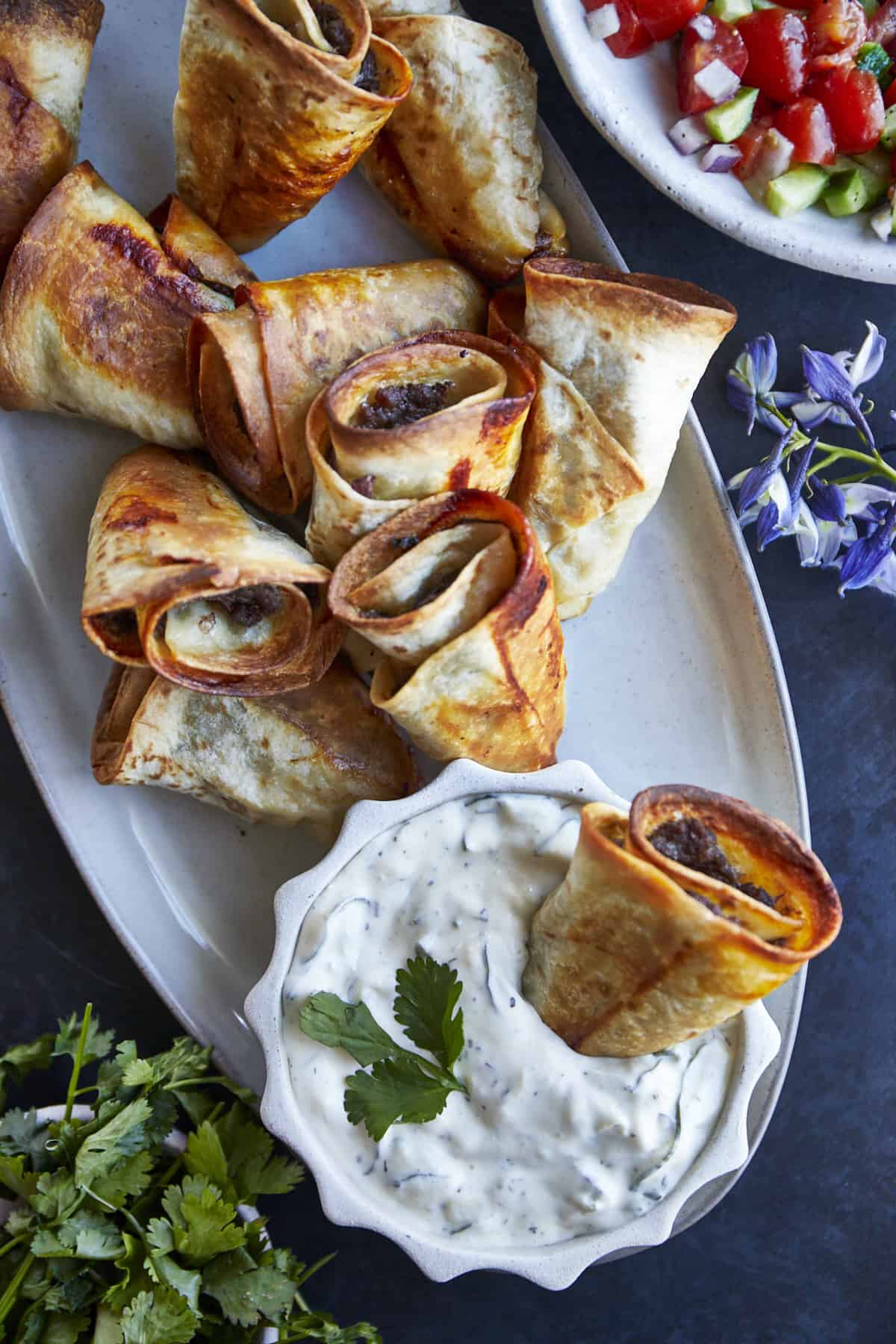 A platter of beef rolls with a side of tzatziki. 