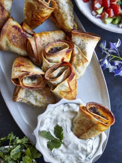 Beef rolls on a platter with a bowl of tzatziki.