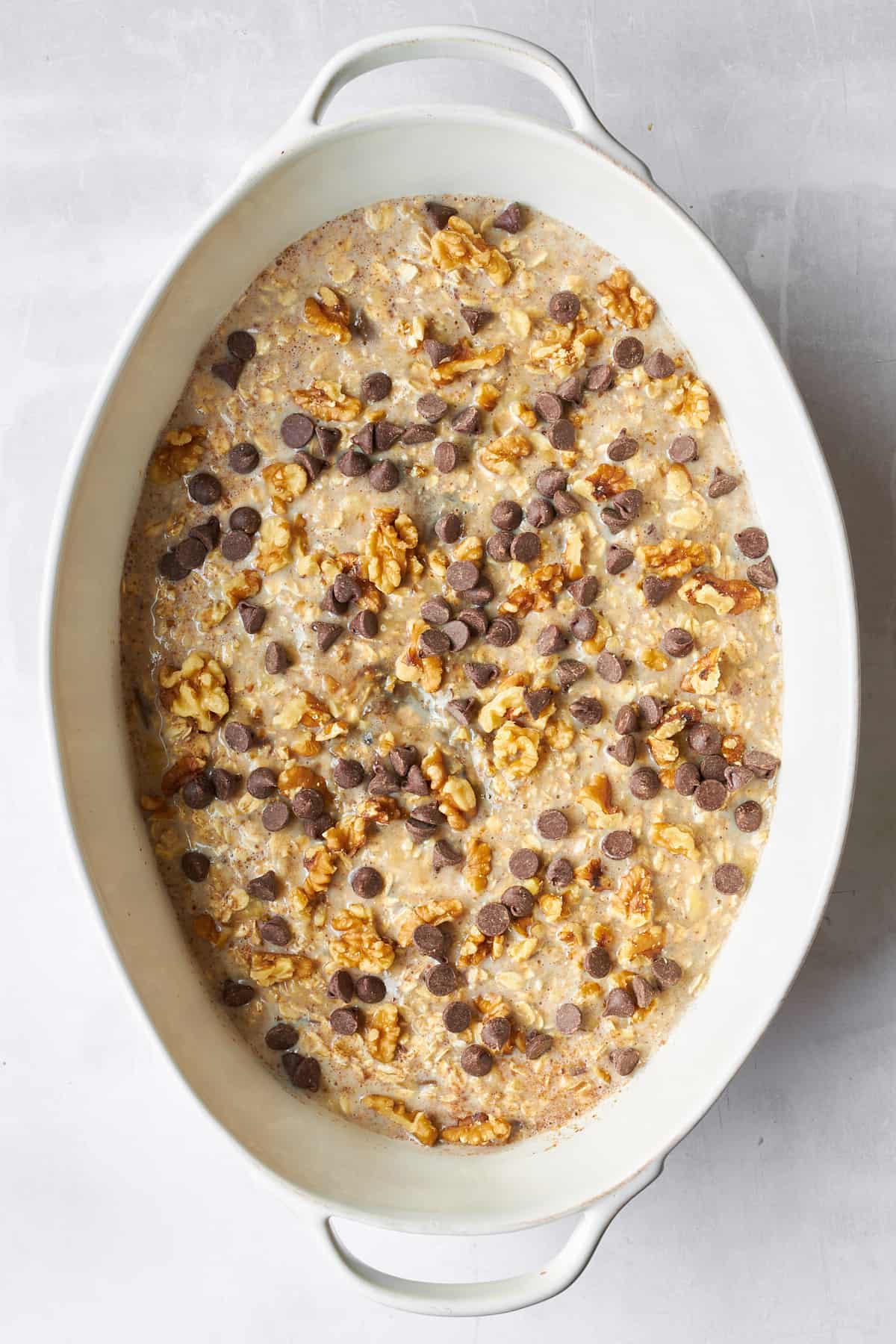 Uncooked banana date oatmeal with chocolate chips in an oval baking dish. 