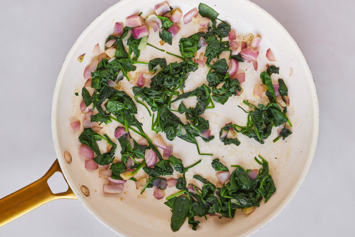 Spinach and shallot being sautéed in a skillet.