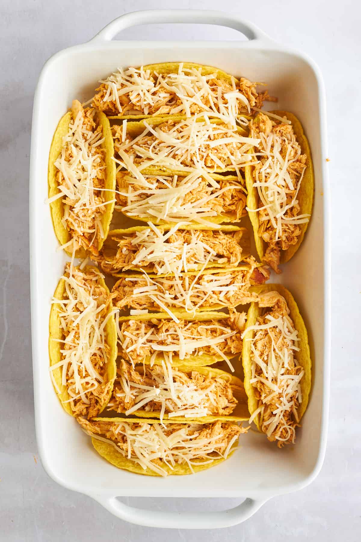 Hard shell tacos in a baking dish stuffed with shredded chicken shawarma and cheese. 
