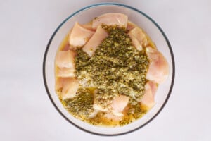 Raw chicken pieces marinading in a bowl of souvlaki marinade.