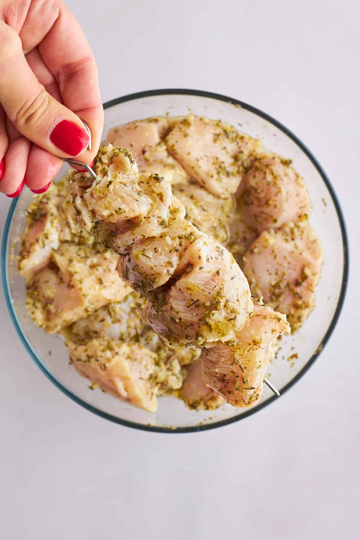 Raw chicken souvlaki being threaded onto skewers. 