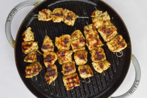 Greek chicken souvlaki skewers cooking on a grill pan.