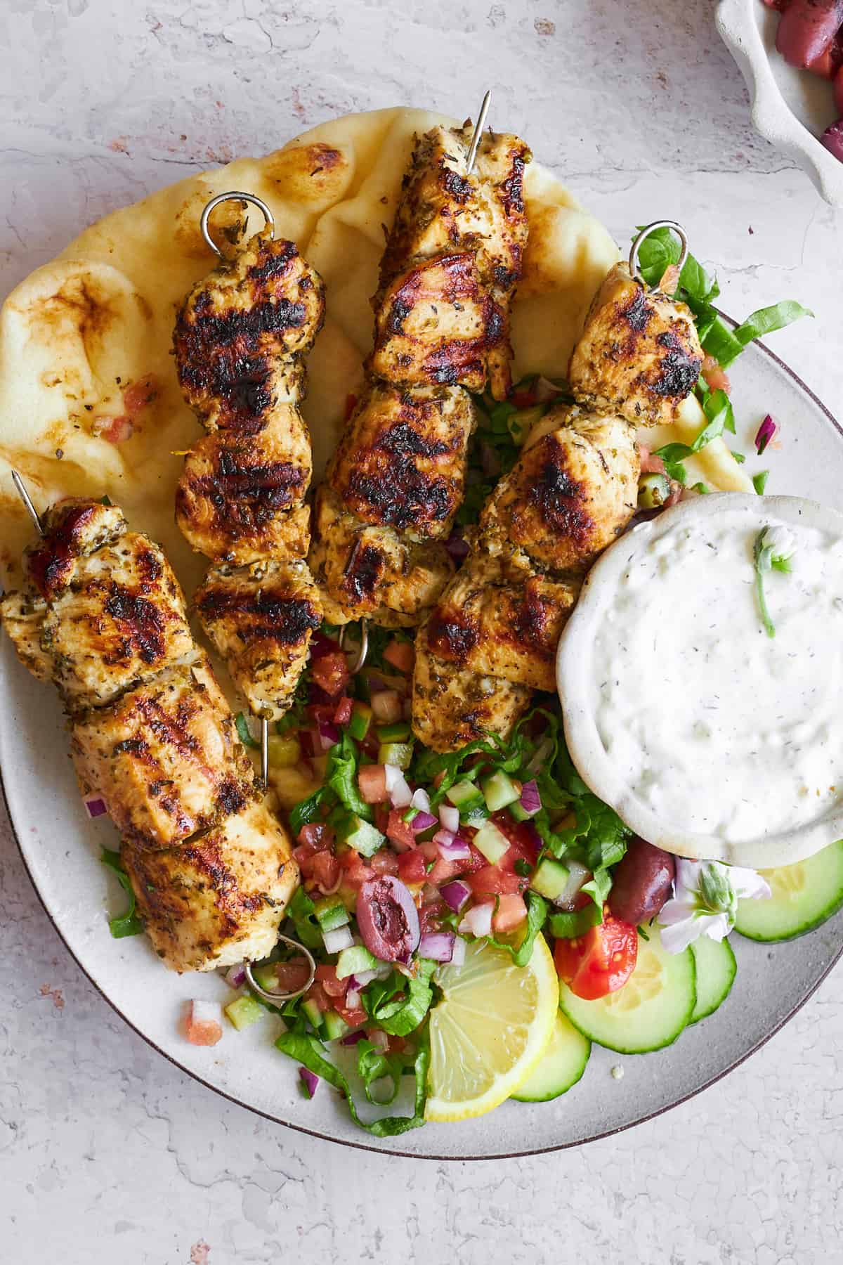 A plate of Greek chicken souvlaki skewers with salad, naan bread, and tzatziki. 
