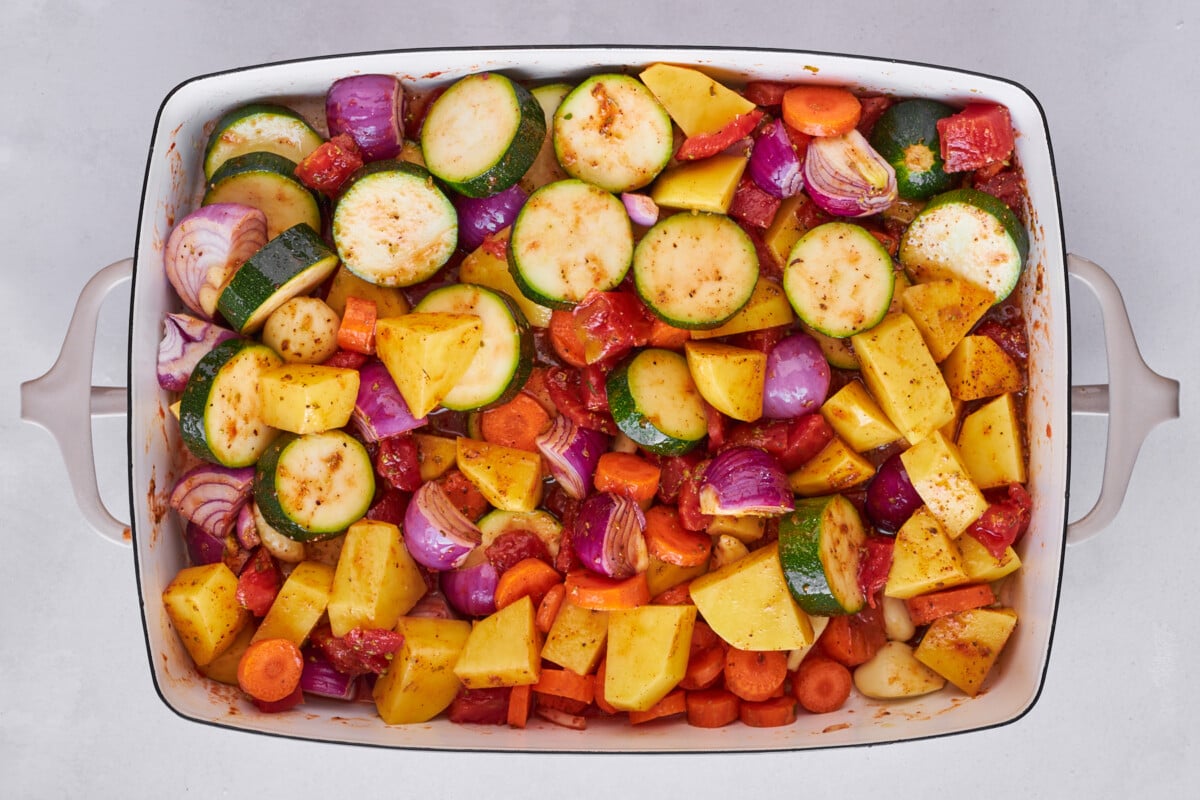 Zucchini, bell peppers, onions, tomatoes, and spices in a baking dish.