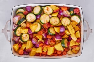 Zucchini, bell peppers, onions, tomatoes, and spices in a baking dish.