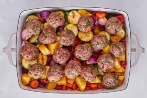 Raw beef kofta meatballs over veggies in a baking dish.