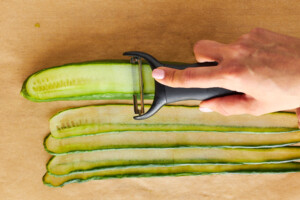 A cucumber being sliced into strips.