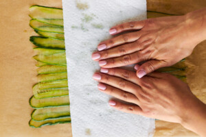 Hands using a paper towel to dry cucumber strips.