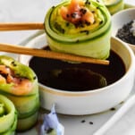 A smoked salmon cucumber roll being dipped in soy sauce.