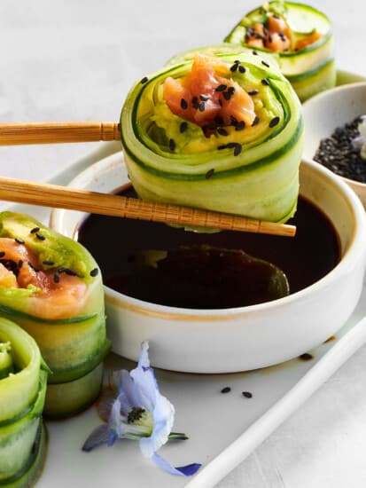 A smoked salmon cucumber roll being dipped in soy sauce.