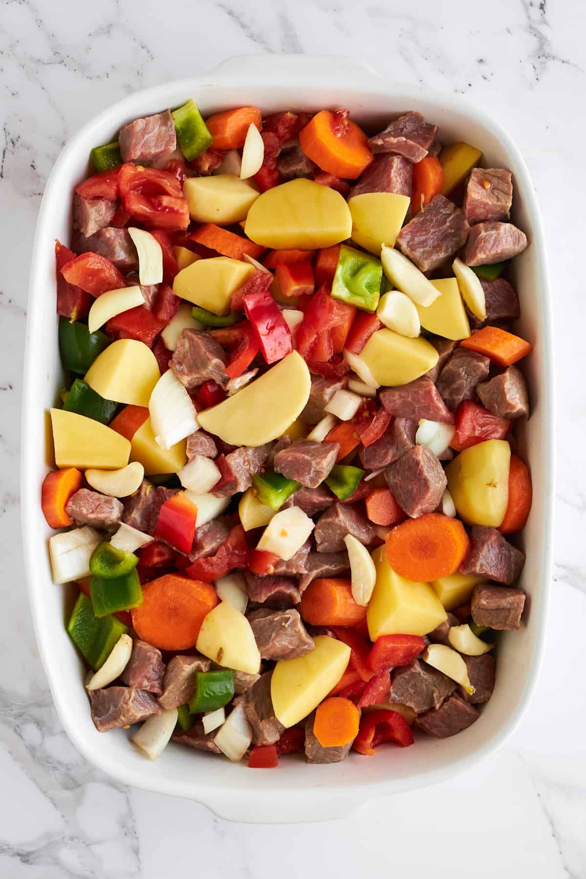 Beef cubes and vegetables in a baking dish.