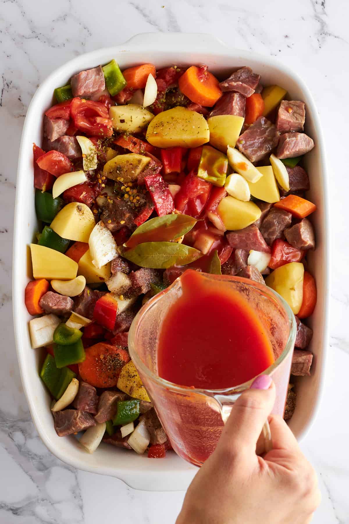 Sauce being poured over beef and vegetables in a baking dish. 