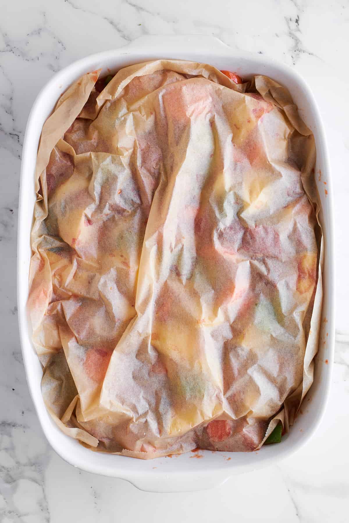 A casserole dish full of beef and veggies topped with parchment paper. 