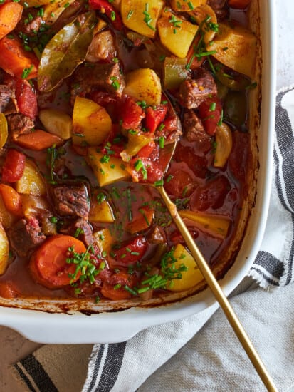A serving spoon in a casserole dish of baked beef stew.