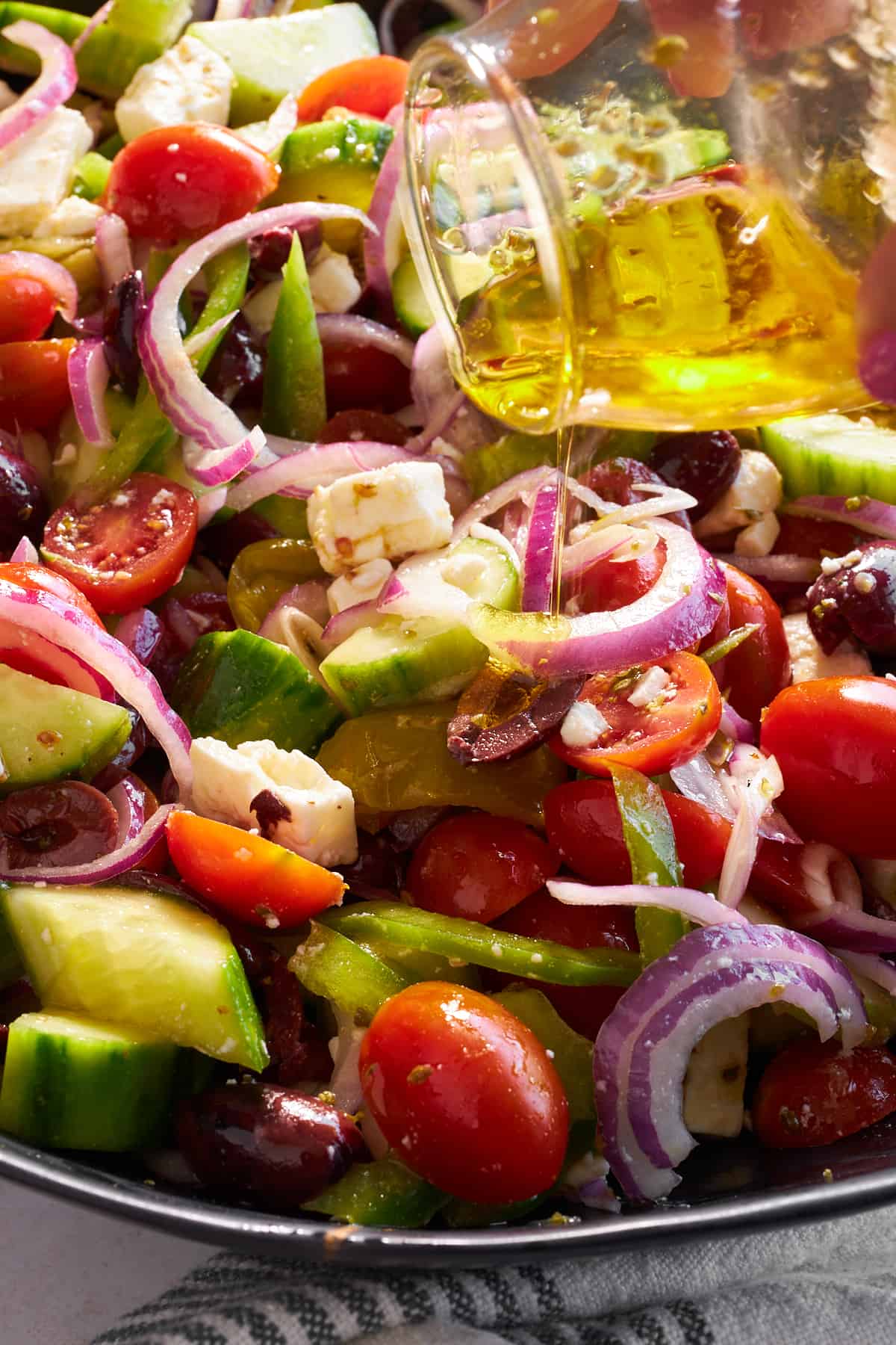 Vinaigrette being poured over a Greek salad. 