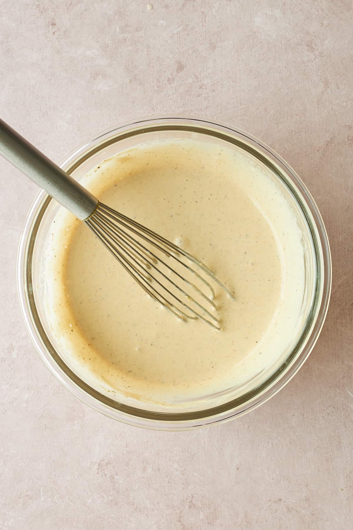 A bowl of tahini dressing with a whisk sticking out. 