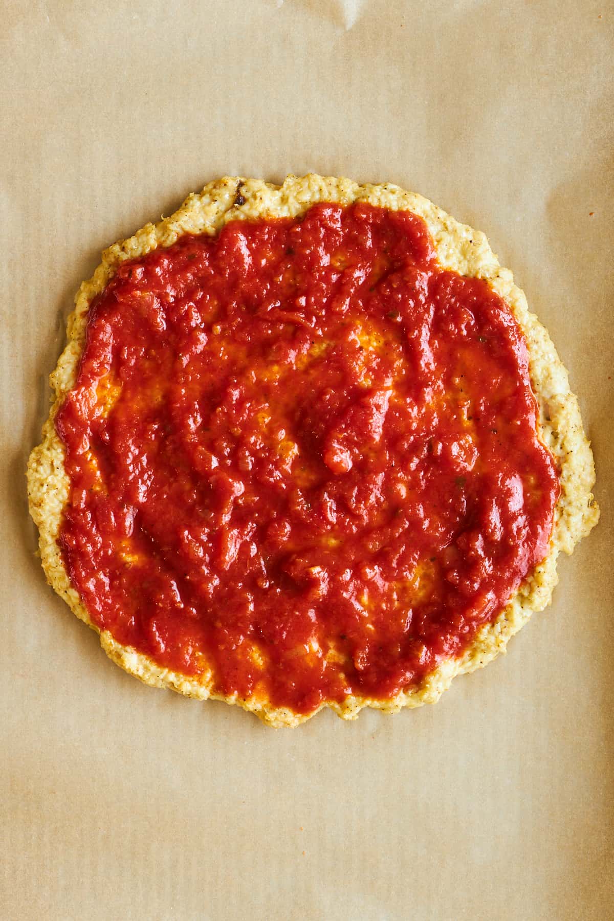 Chicken pizza crust topped with marinara sauce. 