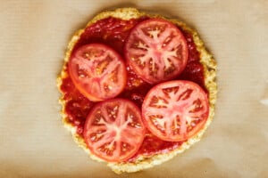 Tomato slices on top of marinara sauce on chicken pizza crust.