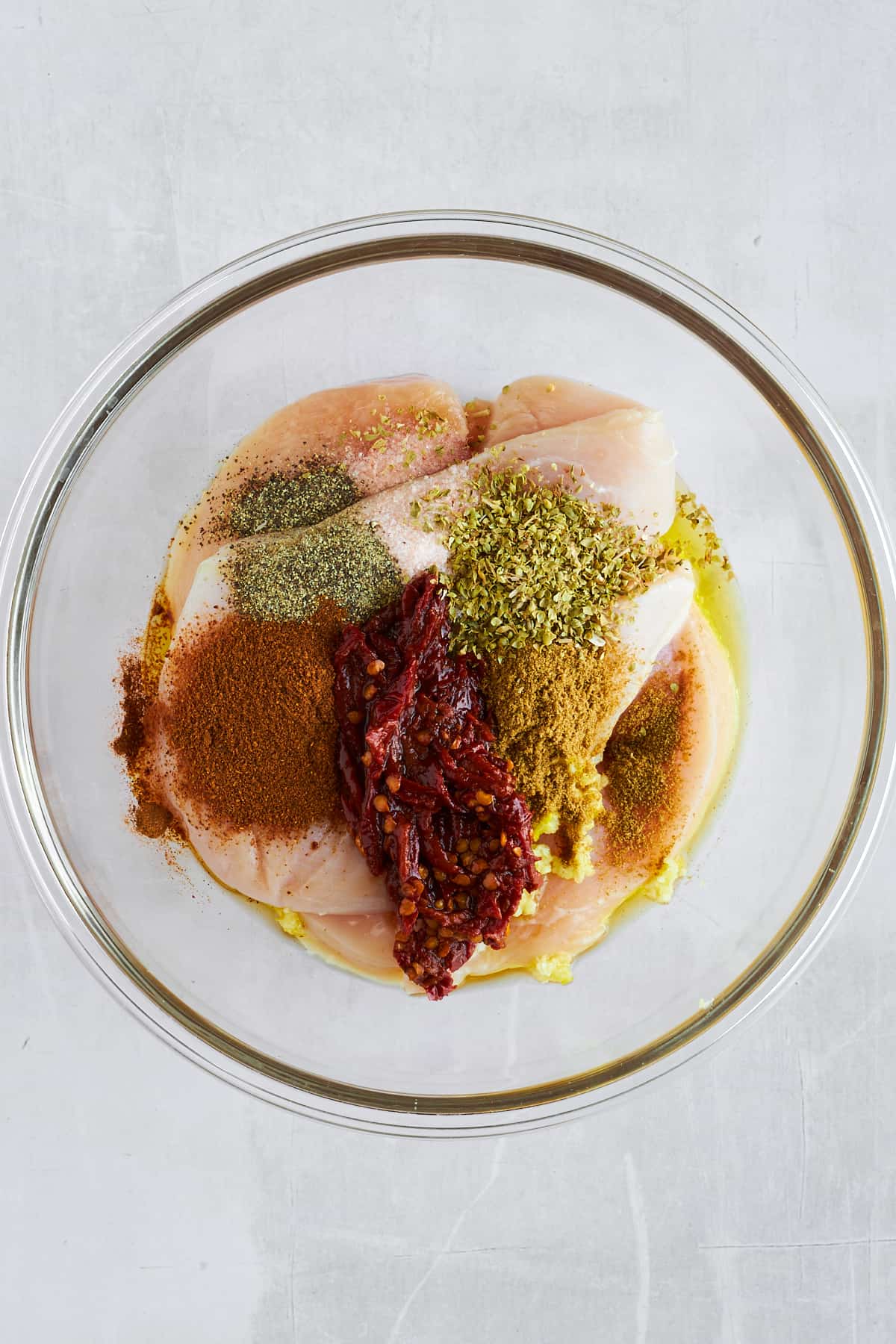 Raw chicken thighs topped with seasonings and oil in a bowl. 