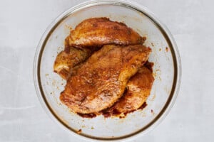 Raw chicken thighs tossed with seasonings in a bowl.