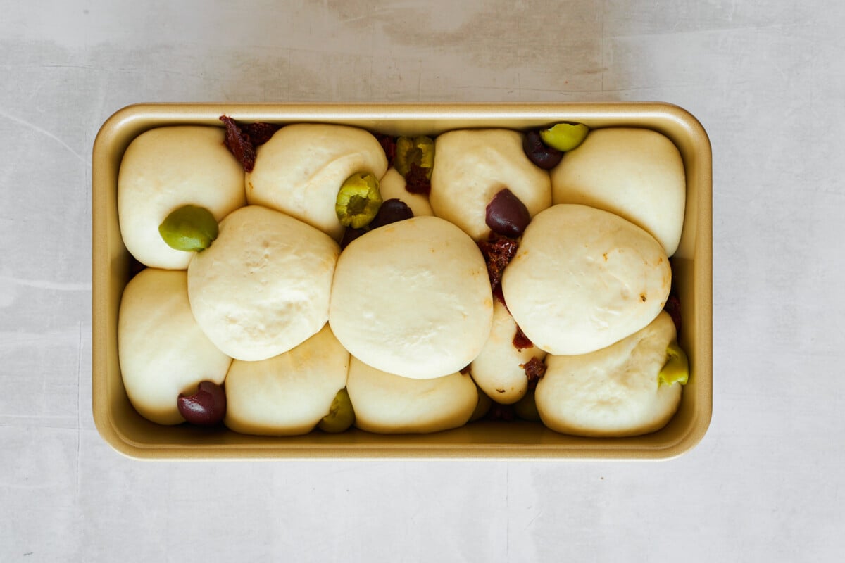 Raw dinner rolls topped with kalamata olives and sun-dried tomatoes.