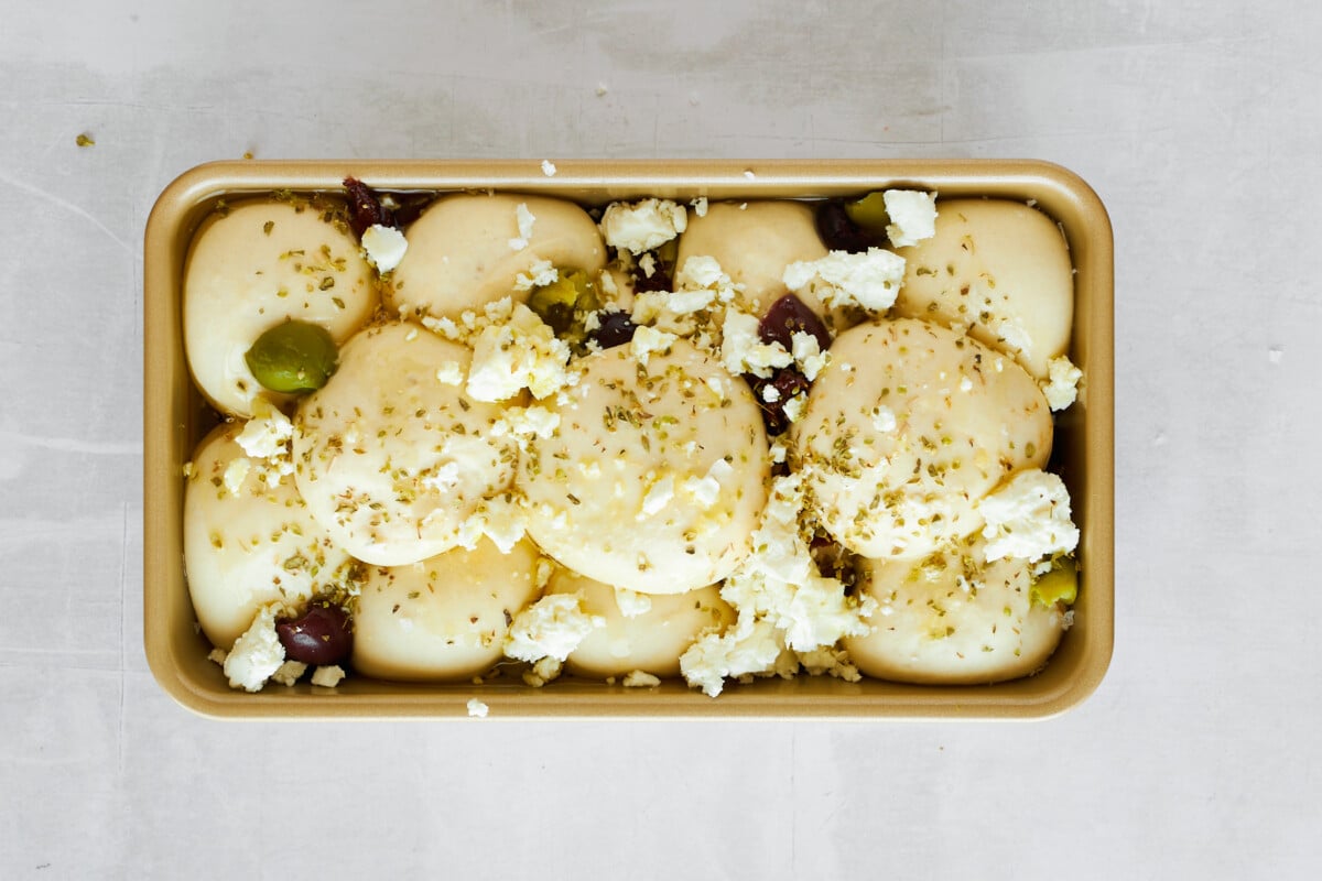 Raw dinner rolls topped with kalamata olives and sun-dried tomatoes and feta.