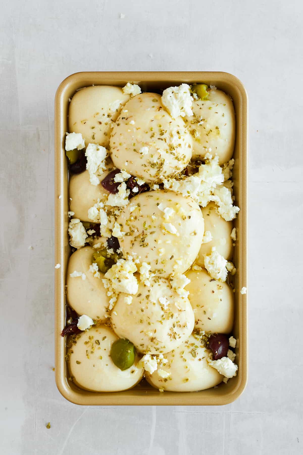 Risen bread rolls, olives, sun-dried tomatoes, and feta in a bread pan. 