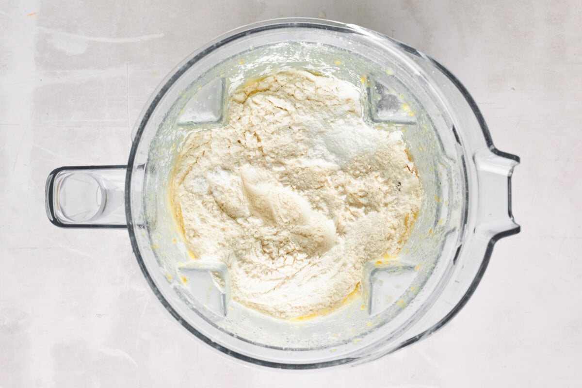 Dry ingredients being added to wet ingredients in a blender.