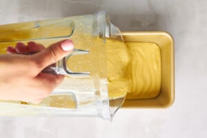 Orange blender cake batter being poured into a loaf pan.