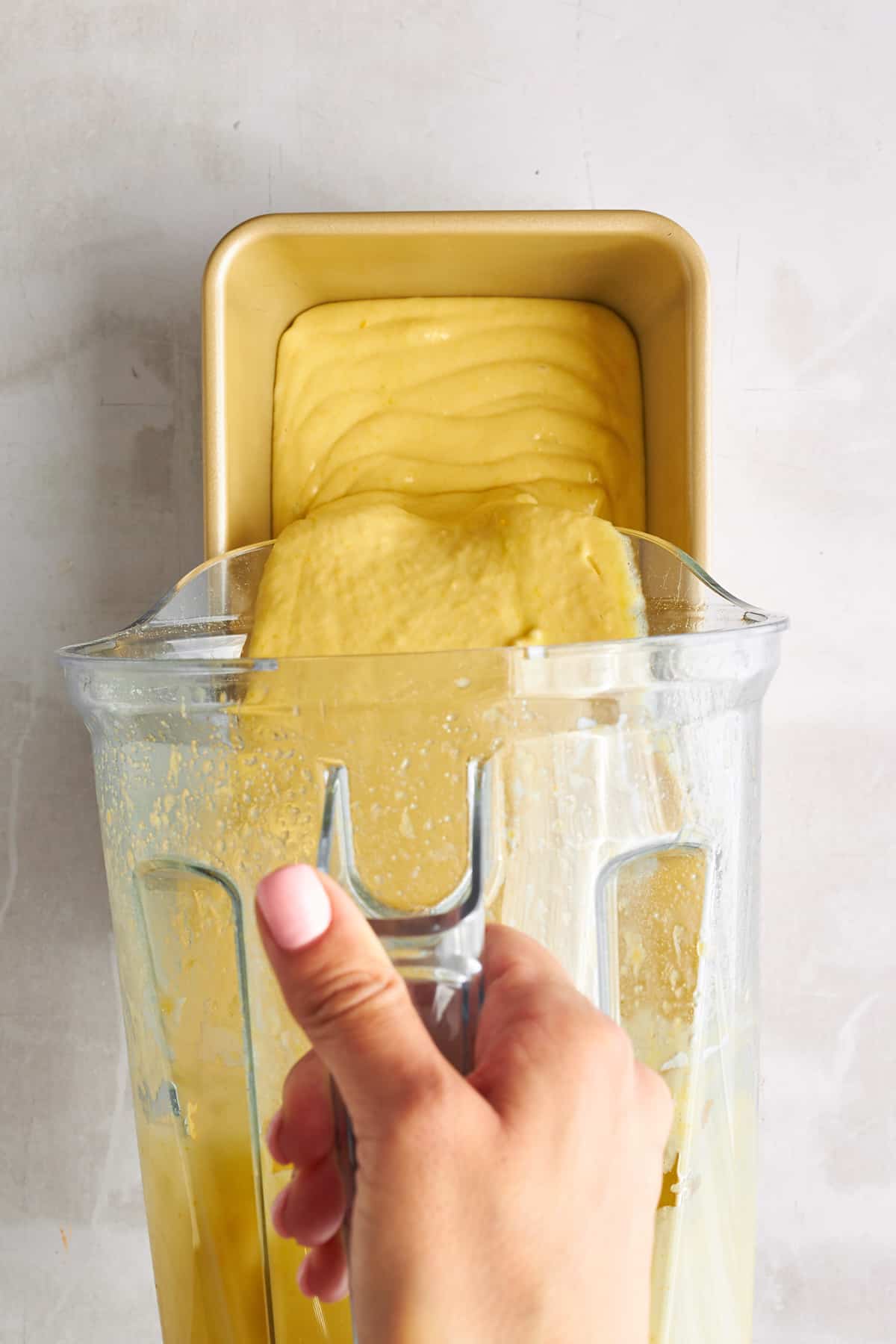 Orange blender cake being poured into a loaf pan. 