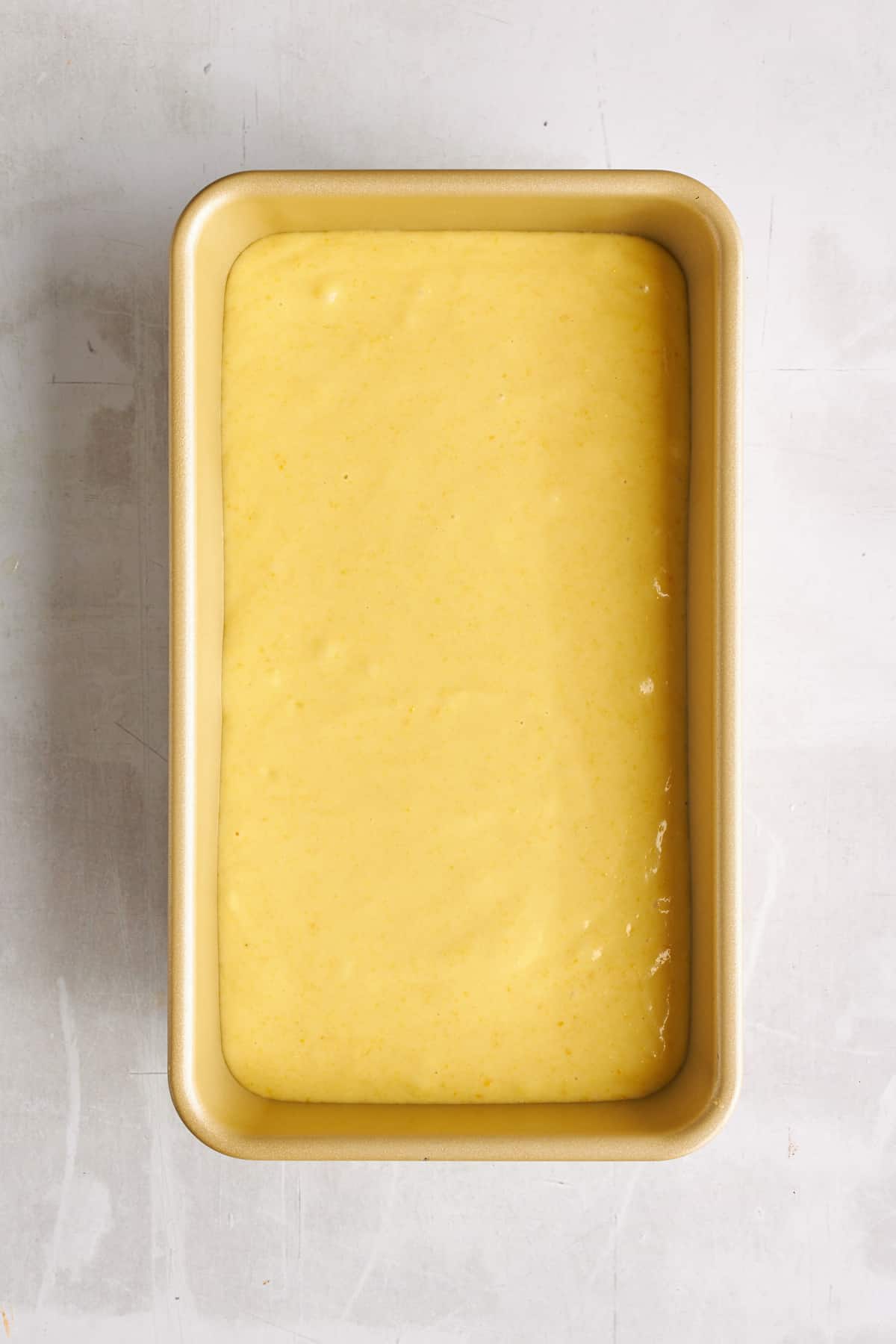A loaf pan full of orange cake batter. 