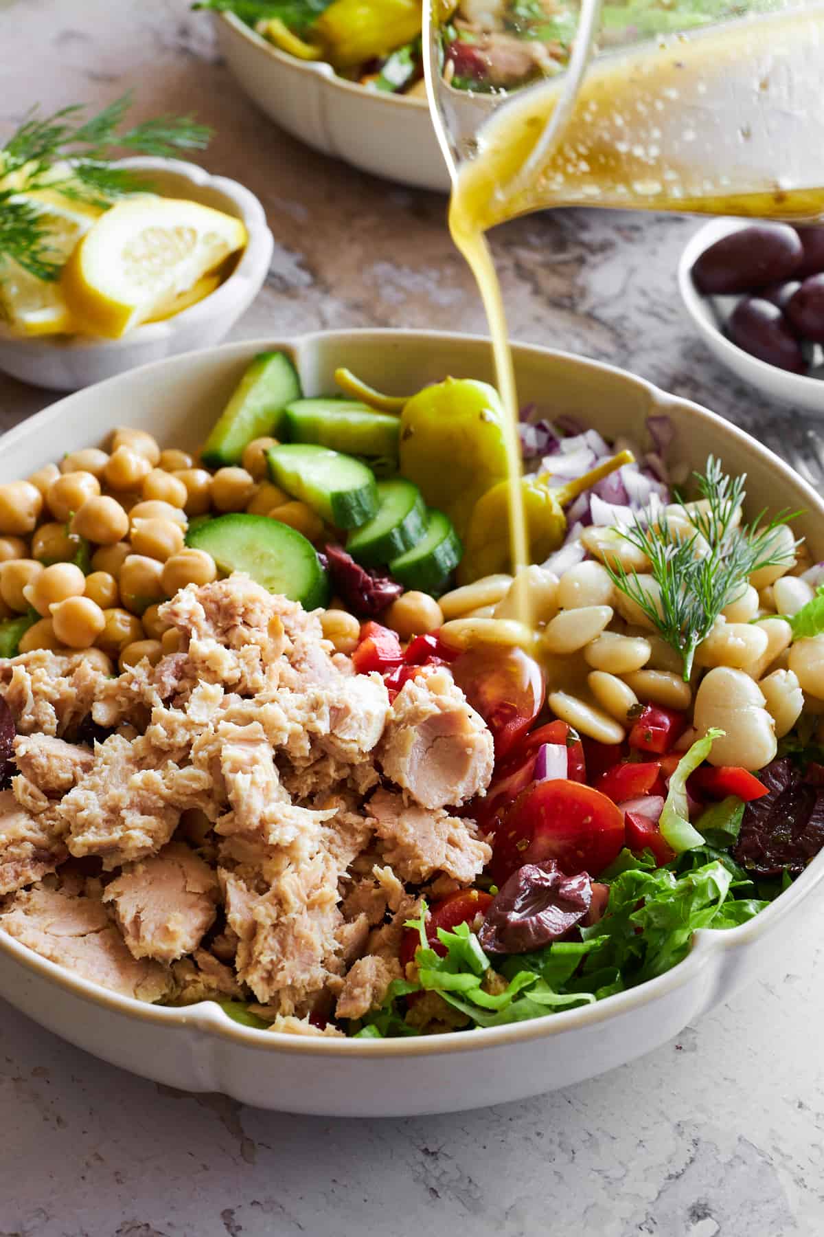 Vinaigrette being poured over a bowl of Mediterranean tuna salad. 